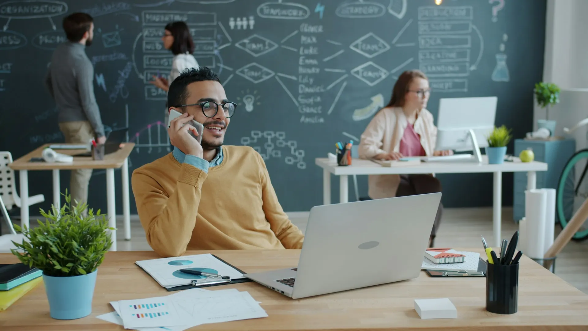 A smiling man talks on his phone at a desk in a modern shared office.