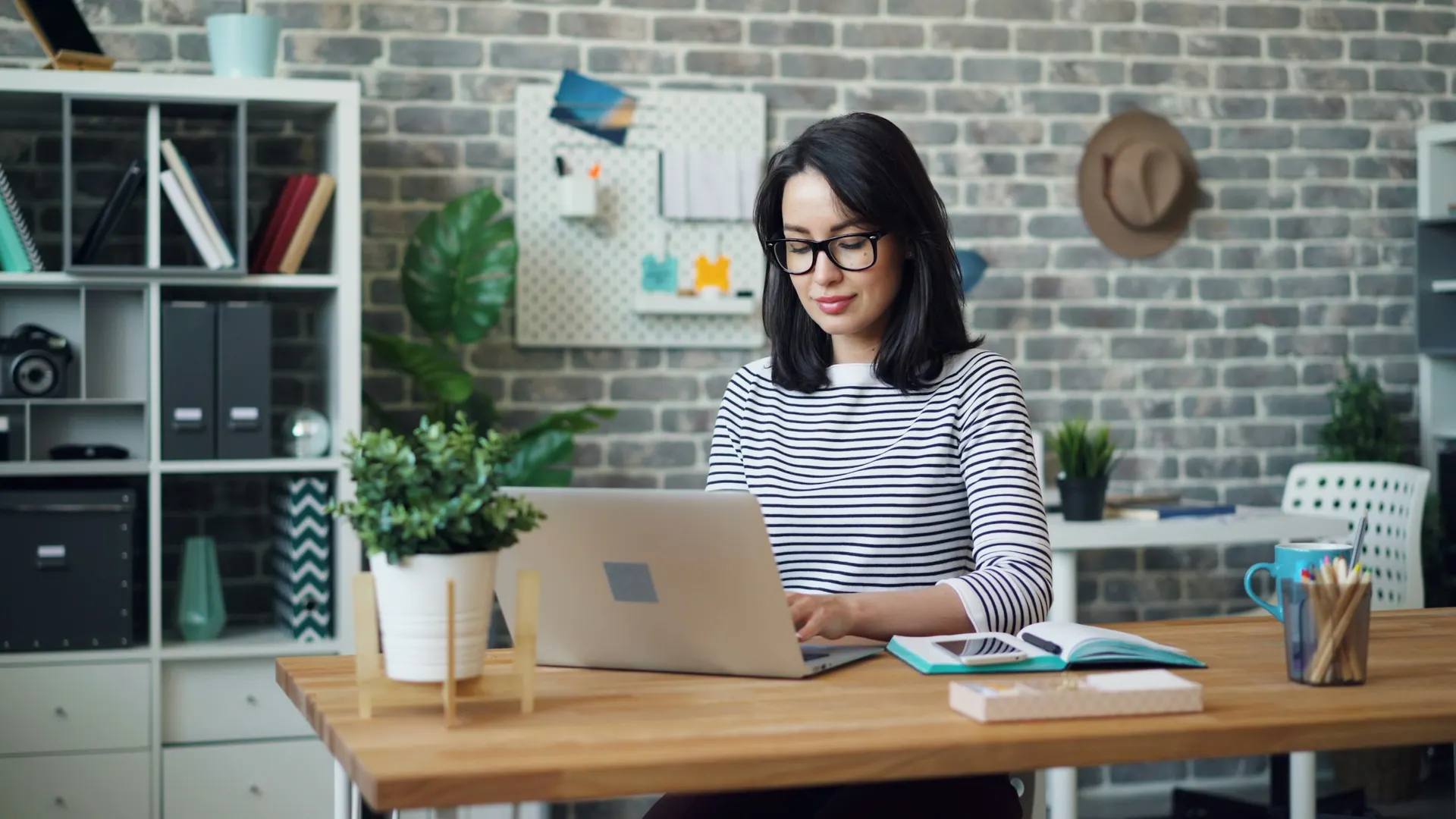 A woman works on a laptop at a wooden desk in a small office.