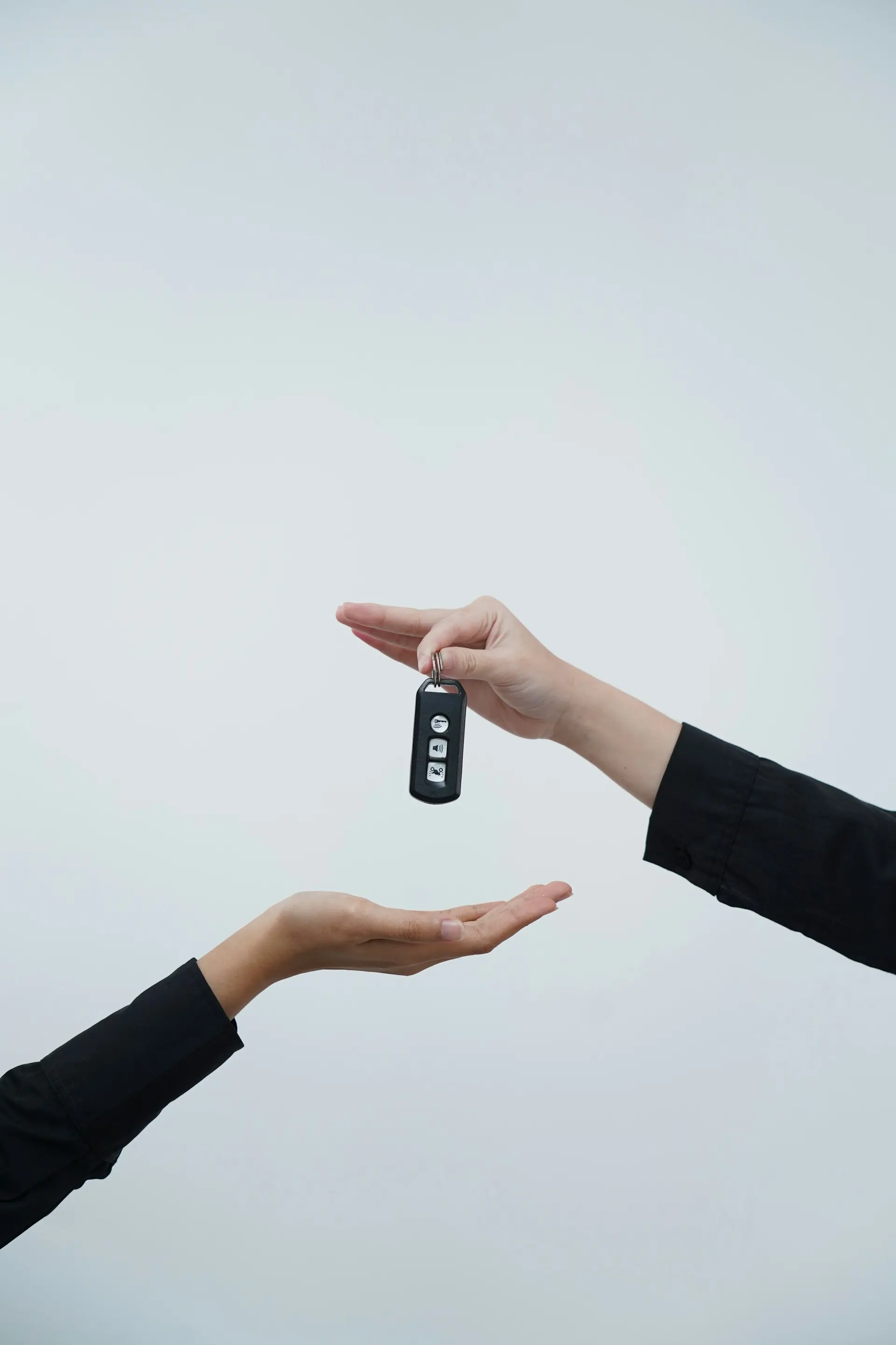 One hand passes a car key to another against a light background.