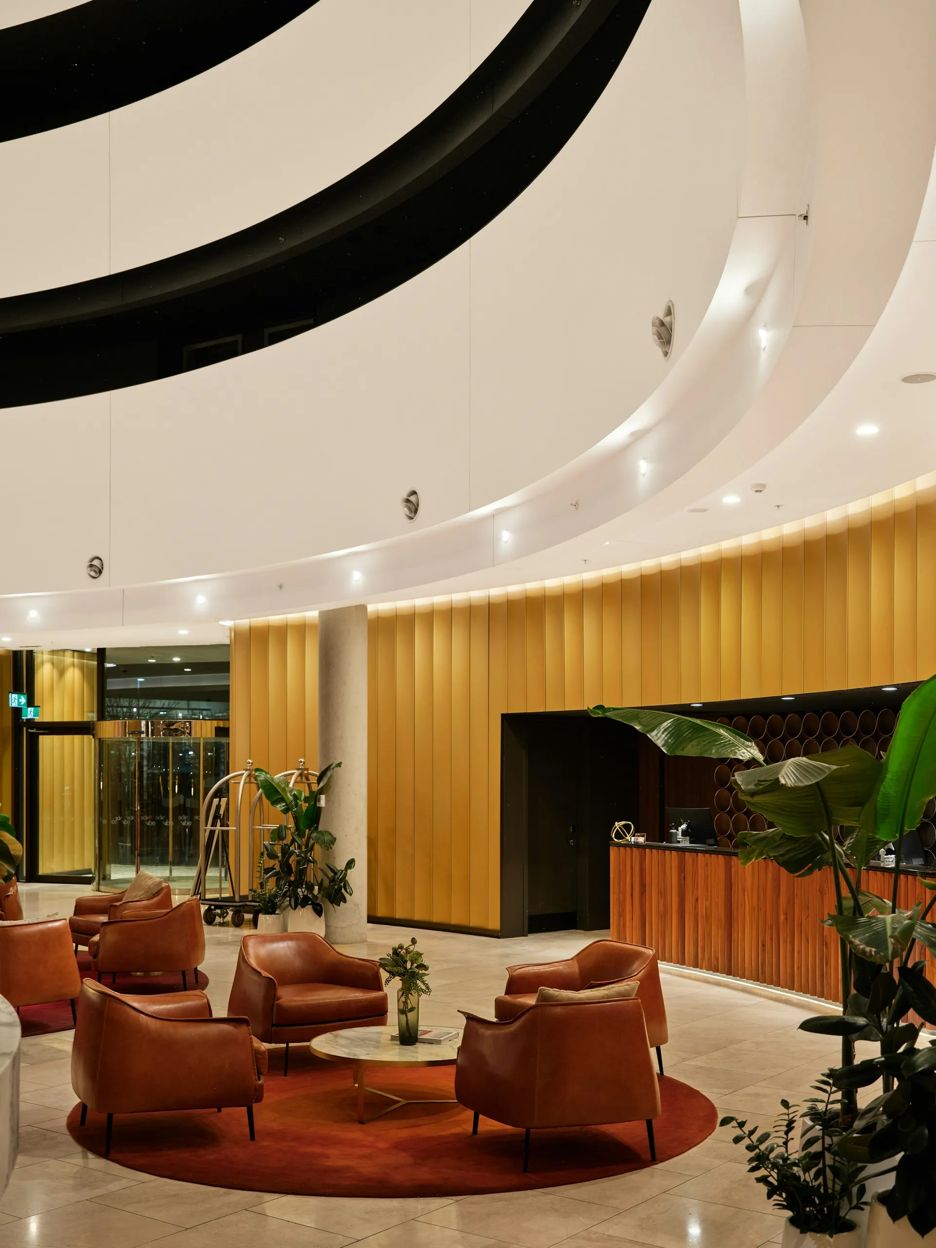A hotel lobby with a reception desk, plants and warm wood panels.