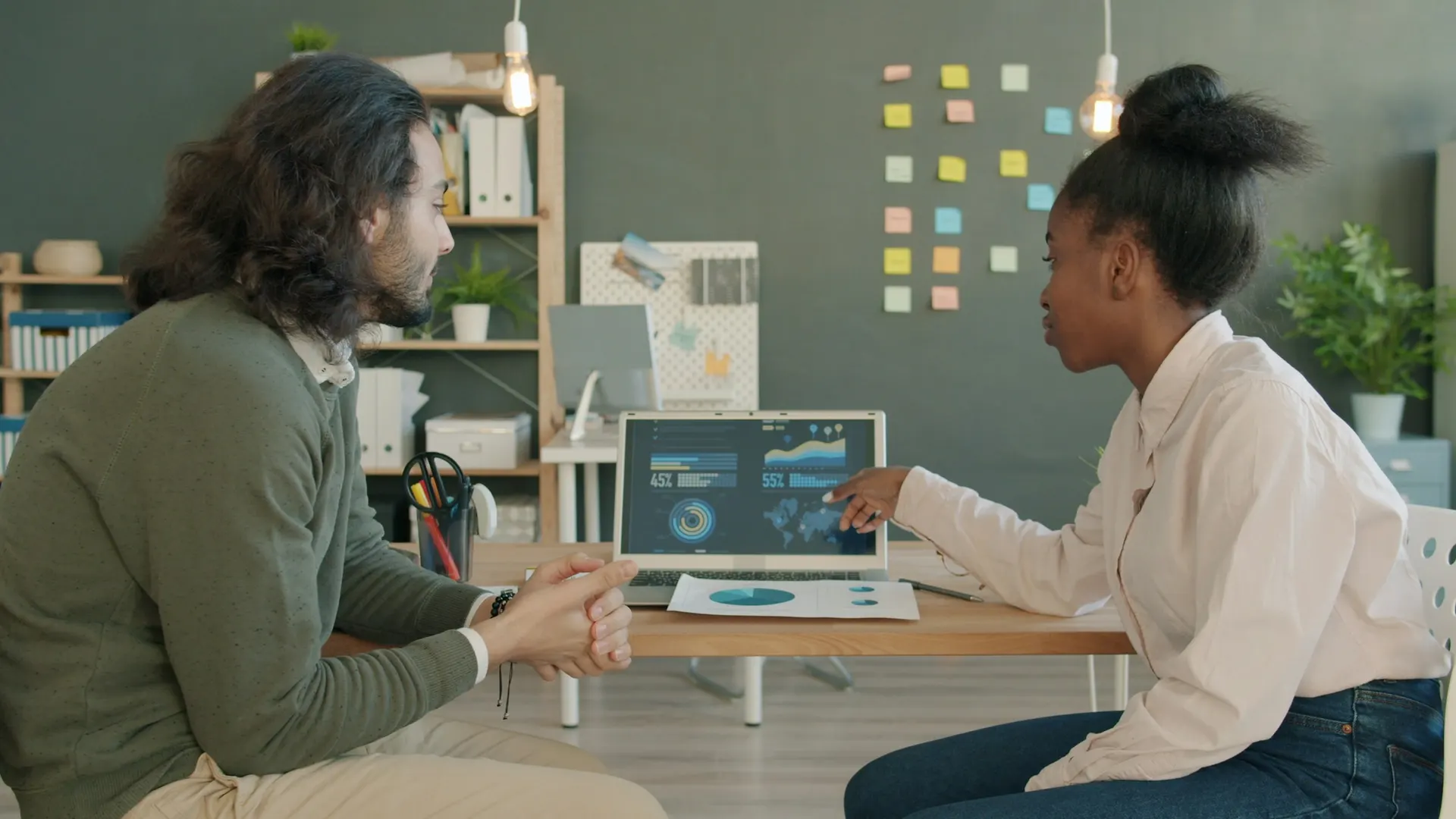 Two colleagues review charts on a laptop in a small office.