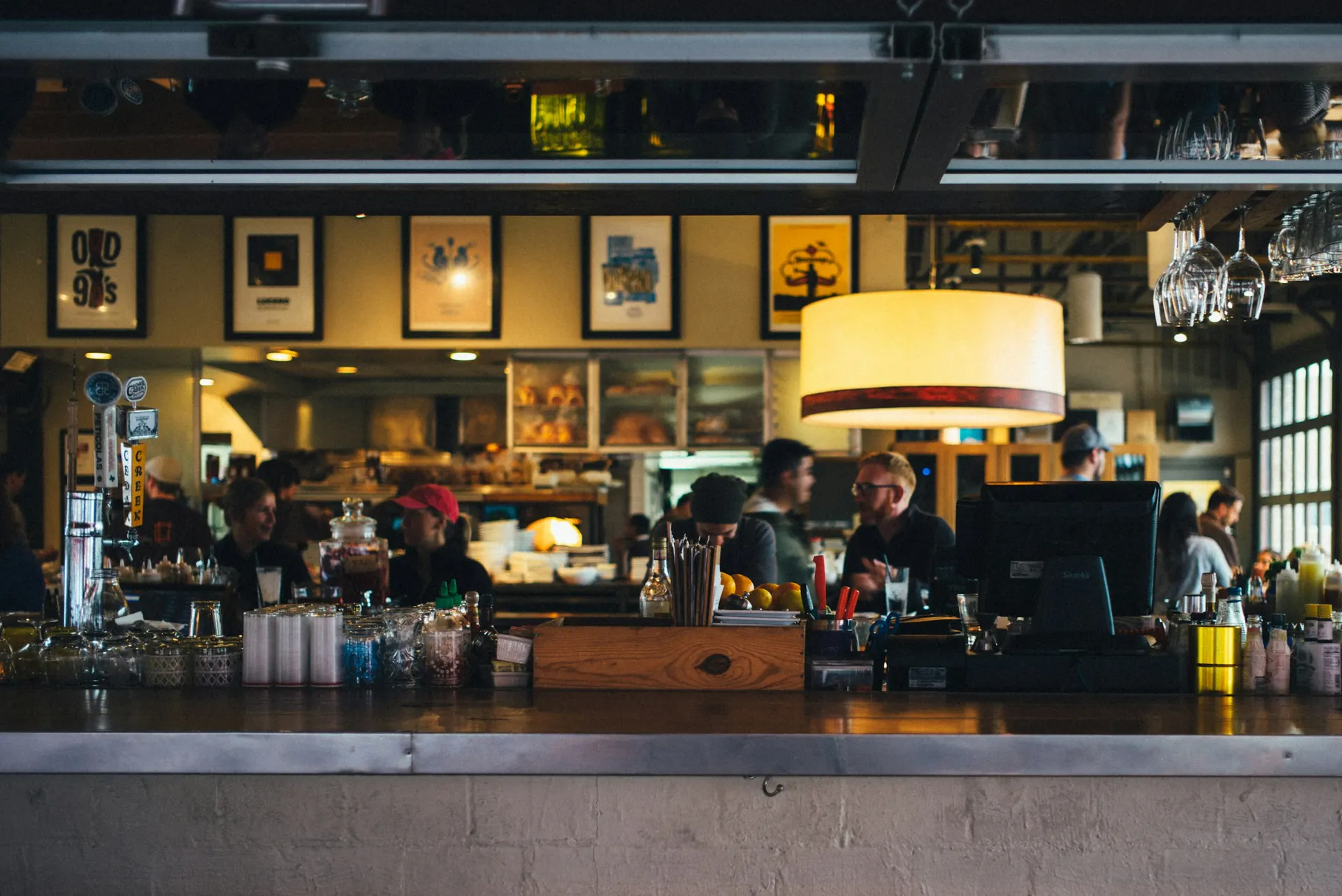 Staff work behind a busy restaurant bar under warm pendant lights.